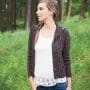 Freeport Cardigan - a brown knitted cardigan pattern. Model is shown standing in a wooded area.