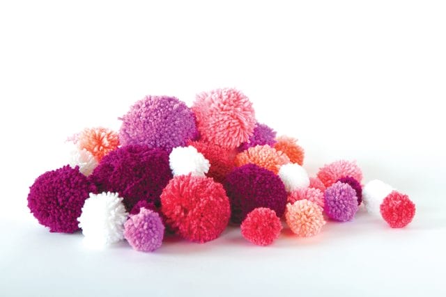 a pile of yarn pom-poms in red, purple, pinks