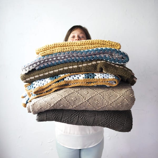 Craft 2 Give Back: A woman holds a large stack of knitted and crocheted blankets in her arms