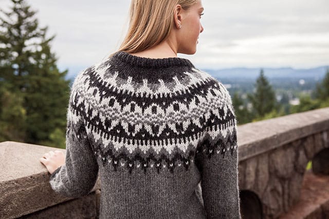 Shown from the back, a woman wears a knitted sweater with an intricate colorwork yoke in grays and white