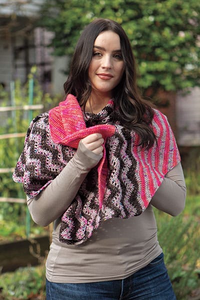 Chevron Pop Shawl - a crochet pattern. A woman is shown wearing a shawl with black and white zigzags and hot pink stripes. Designed by Tian Connaughton for Knit Picks.