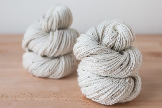 Two hanks of undyed Woodland Tweed yarn on a wooden table