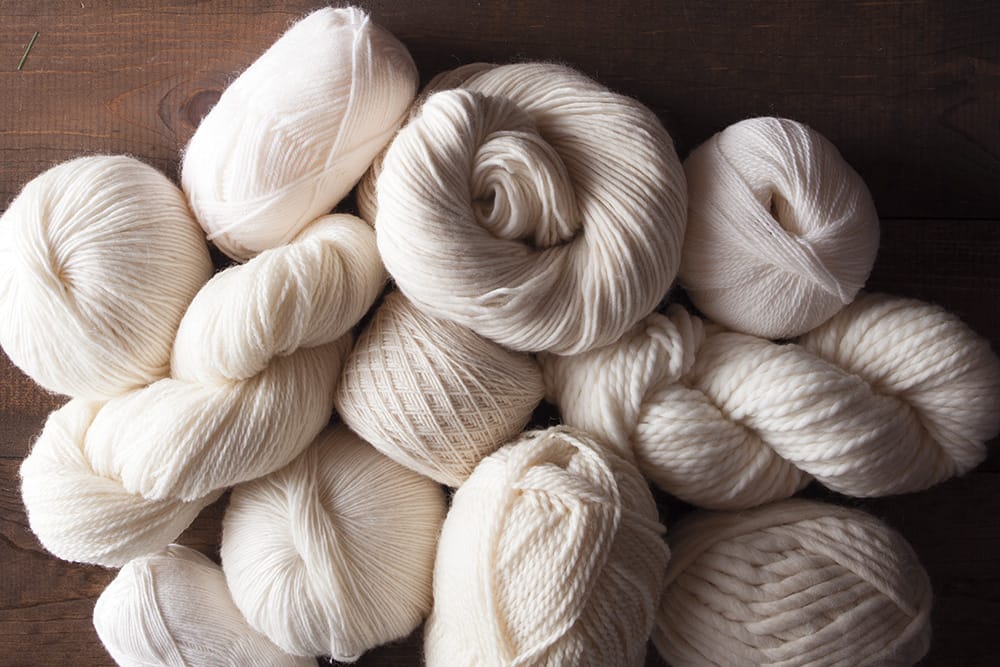 A pile of various undyed yarns on a dark background