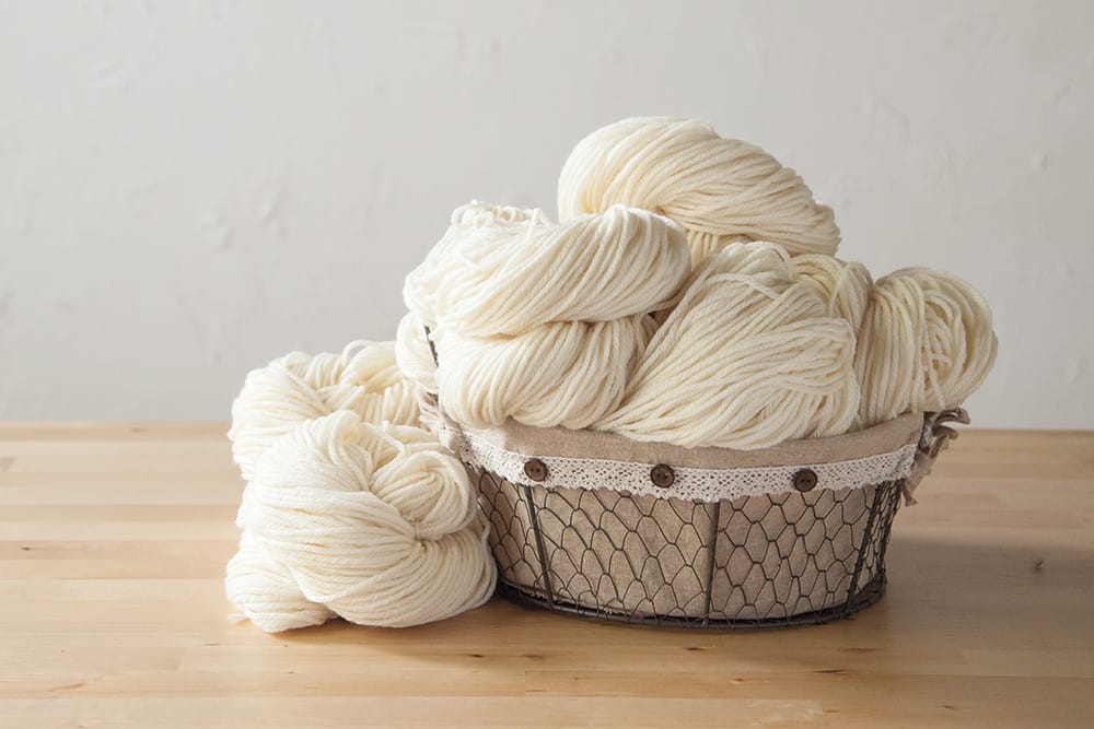 A basket of undyed yarn on a wooden table
