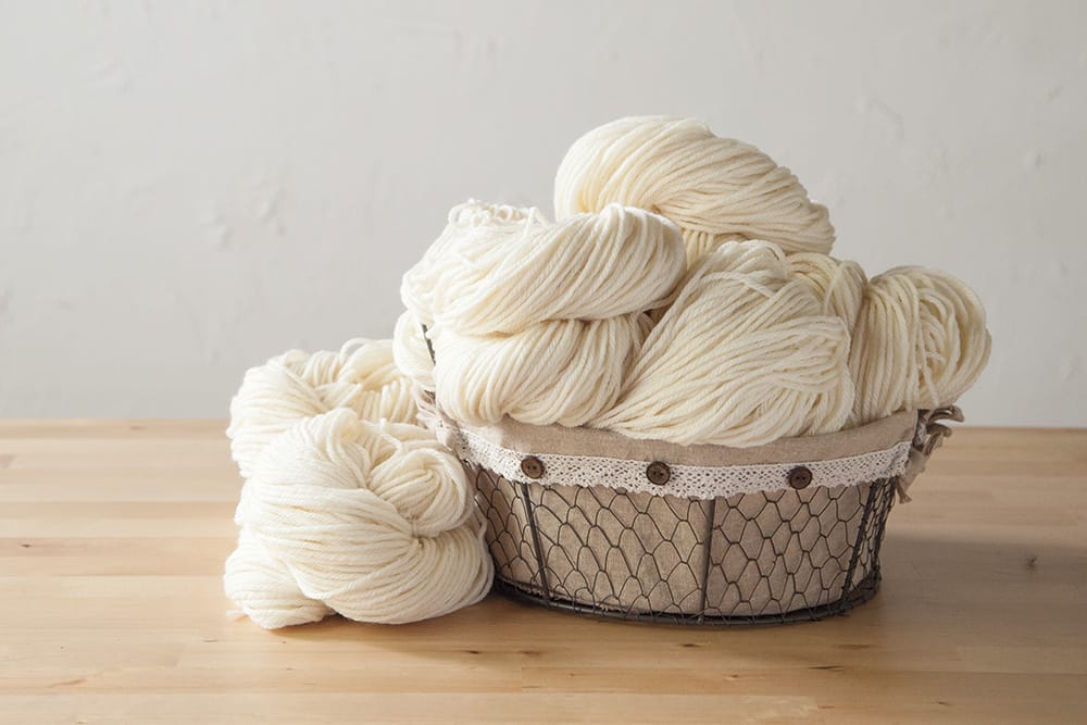 A basket of undyed yarn on a wooden table