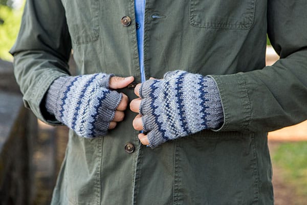 A close up of Jenny Williams' Rye's Stranded Mitts pattern. A model is shown wearing fingerless gloves with stranded colorwork in shades of blue and gray.