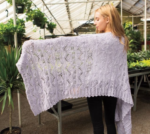 Eden lace shawl - a model is shown wearing a lavender knitted shawl and holding up her yarn to show the stitch pattern.