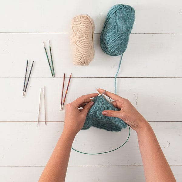Hands knitting on interchangeable knitting needles, surrounded by needle tips and yarn