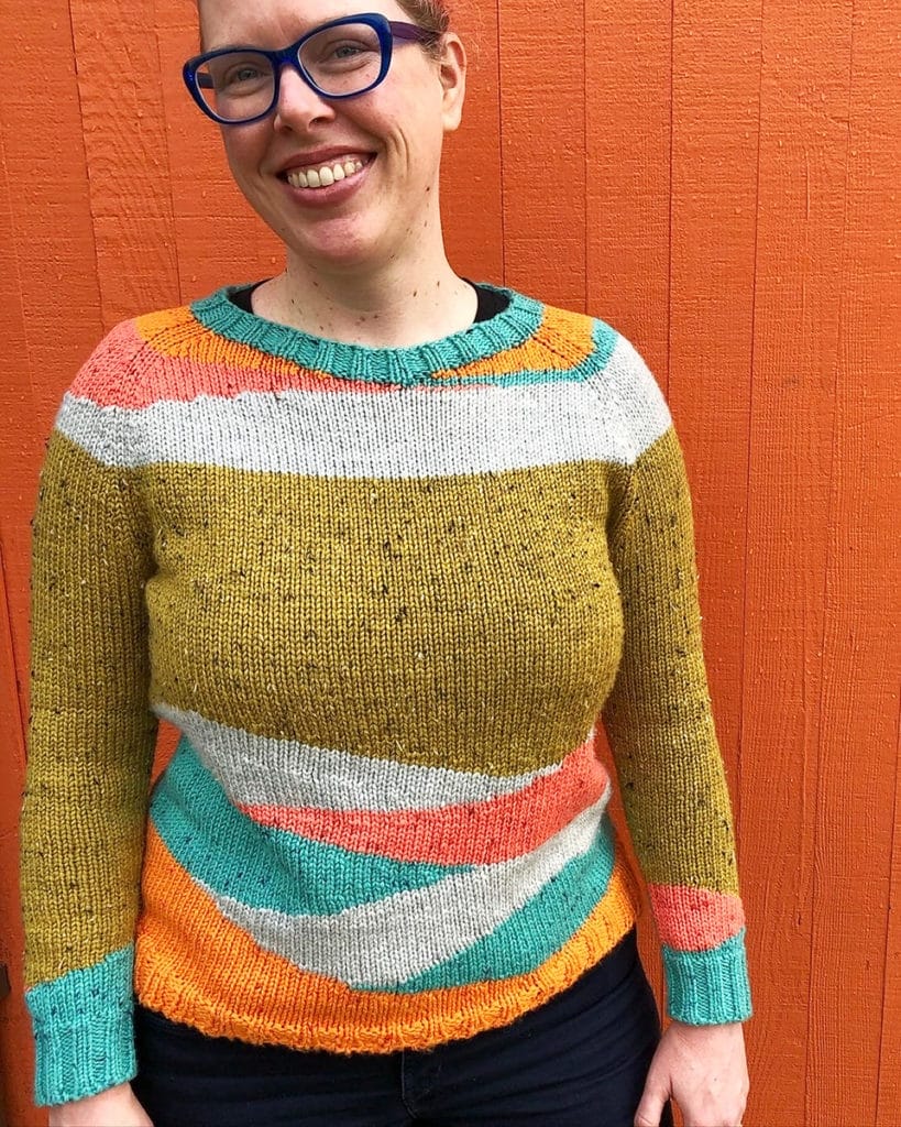 Lee wearing a sweater she made in teal, orange, coral, white, and mustard.