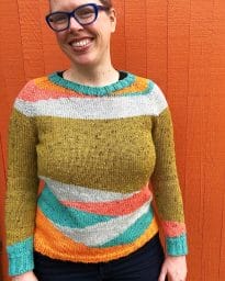 Lee wearing a sweater she made in teal, orange, coral, white, and mustard.