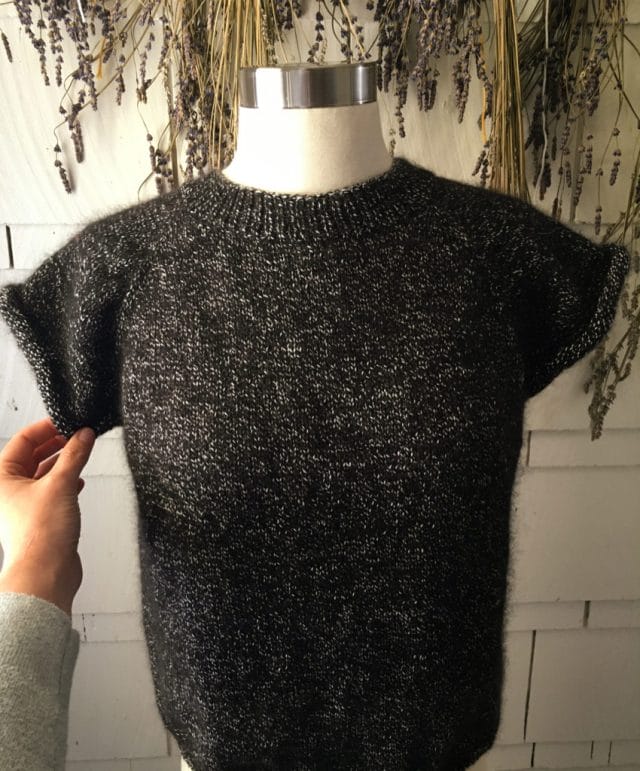 A black and gray knitted sweater is displayed on a dress form.