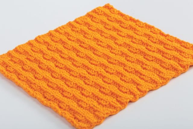 An orange colored knitted dishcloth with an interesting texture.