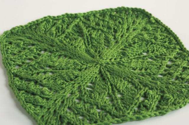 A green knitted dishcloth with a lacy pattern.