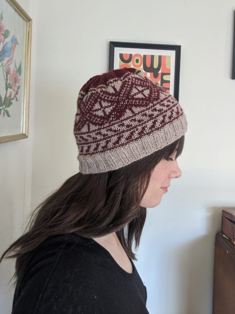 A woman is standing in profile, showing off a knitted hat she made