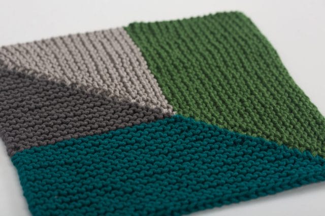 A knitted dishcloth with a color-blocked diagonal pattern in grays and greens.