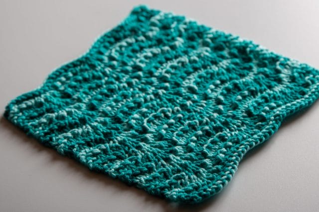 A teal knitted dishcloth with a wavy pattern.