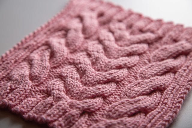 A pink knitted dishcloth with a thick cabled pattern.