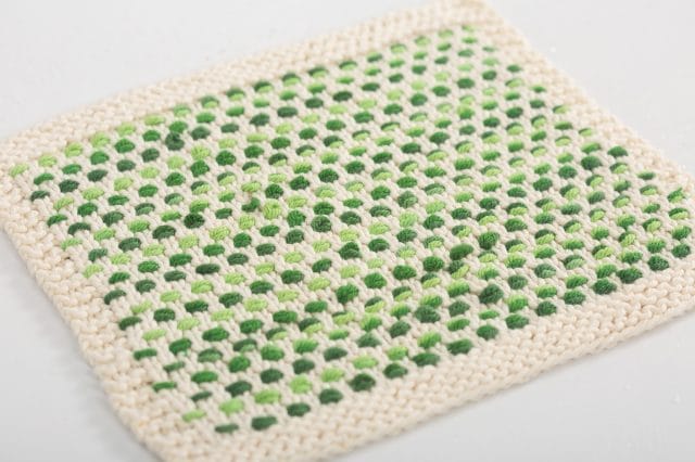An off-white knitted dishcloth with a woven green pattern.