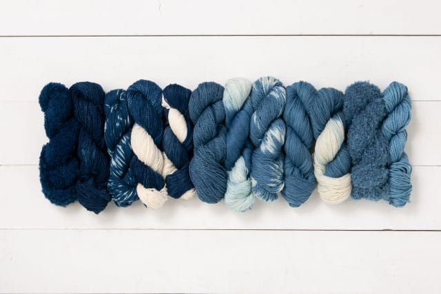 a row of 12 skeins of yarn dyed with indigo, varying in intensity from dark blue to lighter blue