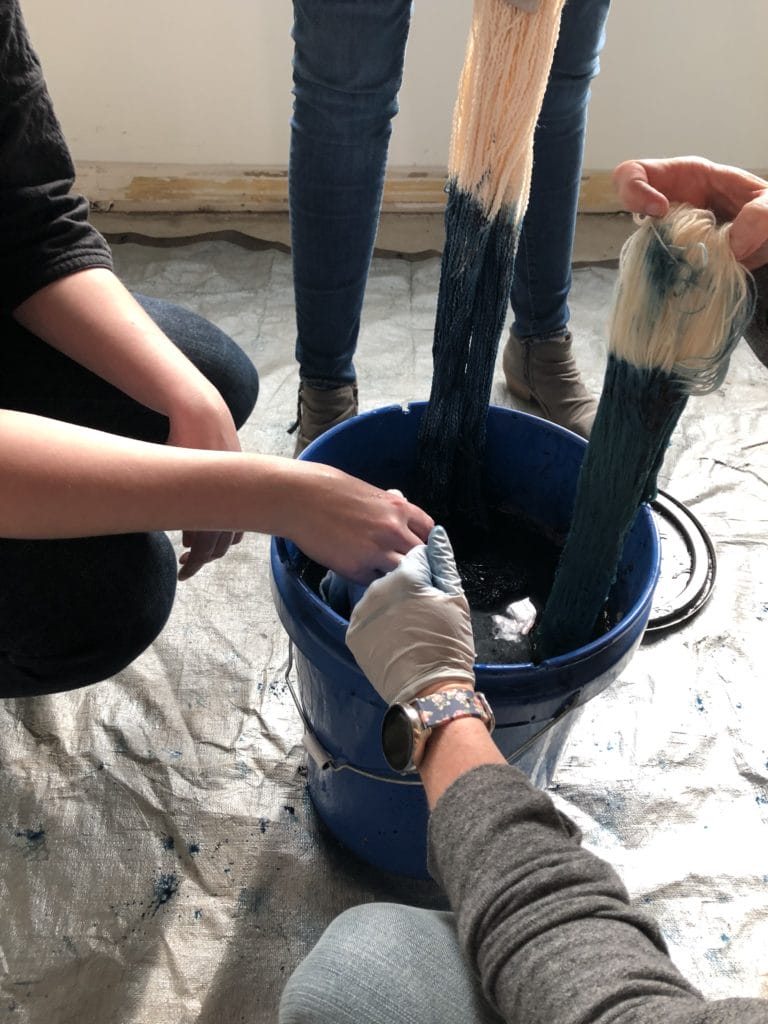 a closeup of the bucket of indigo dye with people dipping skeins of yarn into it