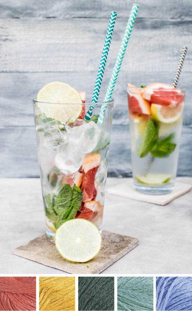 A yummy-looking refreshing beverage in a glass containing ice, mint, blood orange, and lime, topped off with a slice of lemon and two pretty blue paper straws. Beneath is a color palette that consists of five yarn swatches in coral, golden yellow, dark green, sage green, and light blue.