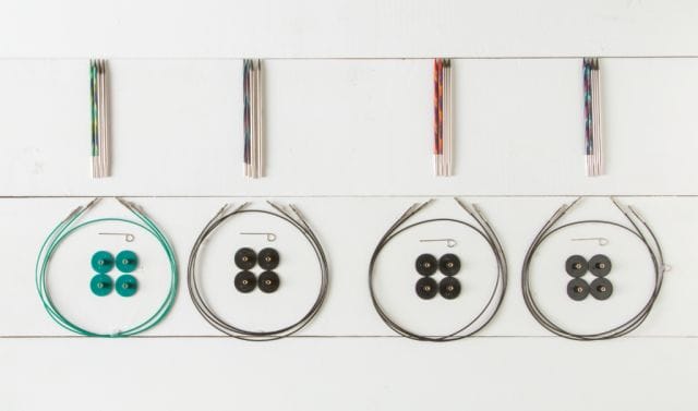On a white board background: Four groups of interchangeable knitting needles along with the cables, caps and keys that go with the sets.
