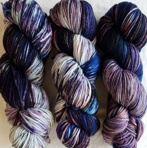 Three hanks of hand-dyed yarn in blackberry, blue, and purple tones.