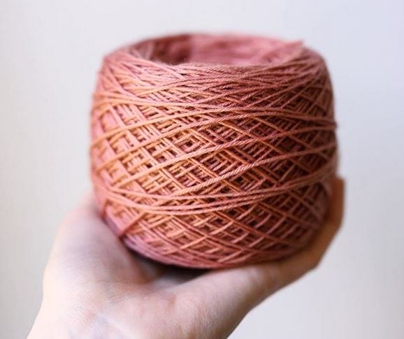 A hand holds a cake of pink yarn - it has been naturally dyed with avocado.