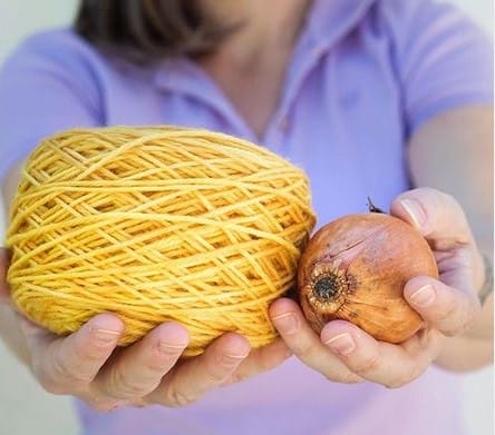 Hands holding a cake of bright yellow yarn and an onion.