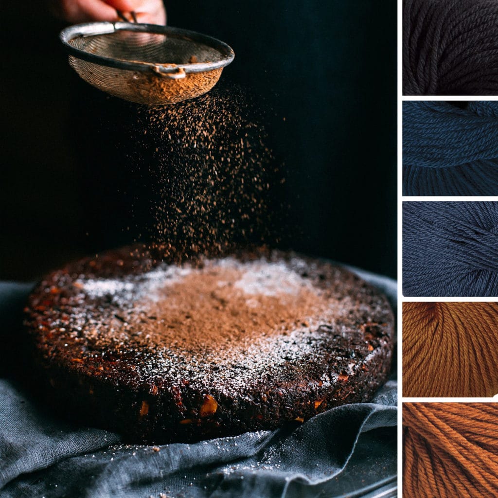 An autumn color palette: To the left, the inspiration photo consists of a dark blue background where a hand is shaking cocoa powder onto a rustic chocolate cake. To the right, five yarn swatches from Gloss yarn in the following colors: Navy blue, dark sea blue, gray blue, gold, and rust.