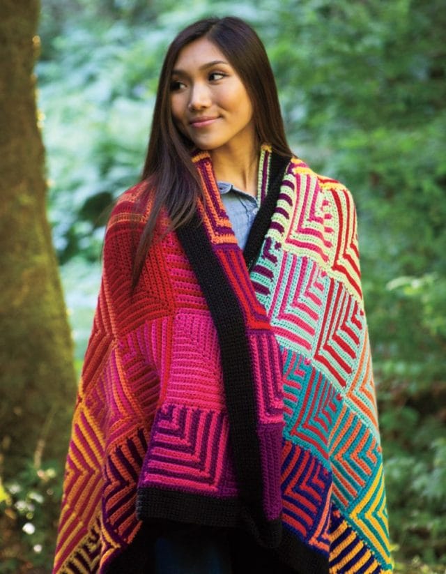 A model is draped in the Hue Shift Afghan - crochet edition.