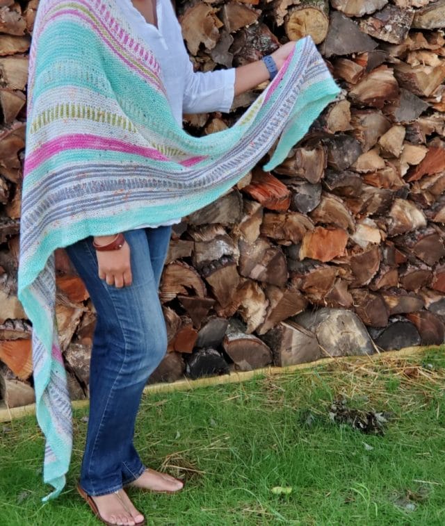 A woman wears a colorful knitted shawl in multicolored teal, hot pink, white speckle, and gray stripes. Color Crazy by Tamy Gore -- A new indie knitting pattern available at knitpicks.com.