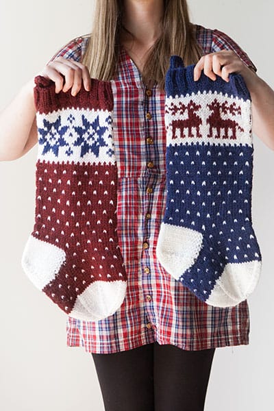 Traditional Fair Isle Holiday Stockings pattern - a model holds two knitted stockings with traditional winter motifs