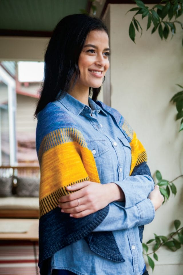 A model wears a blue + yellow knitted shawl, the Koloreak shawl from Knit Picks.