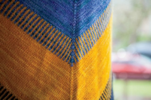 A close-up view of the texture of a blue + yellow knitted shawl, the Koloreak shawl from Knit Picks.