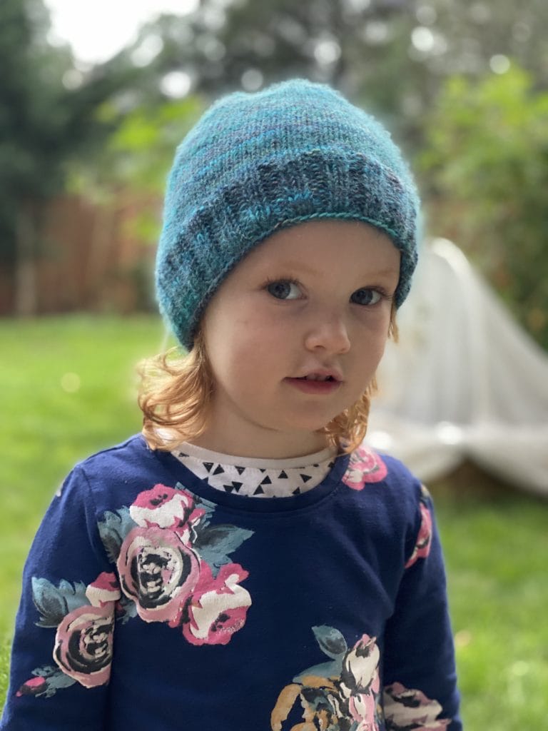 A child wears a fuzzy turquoise knitted hat
