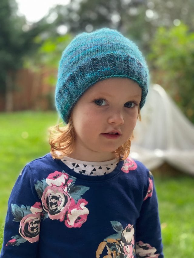 A child wears a fuzzy turquoise knitted hat