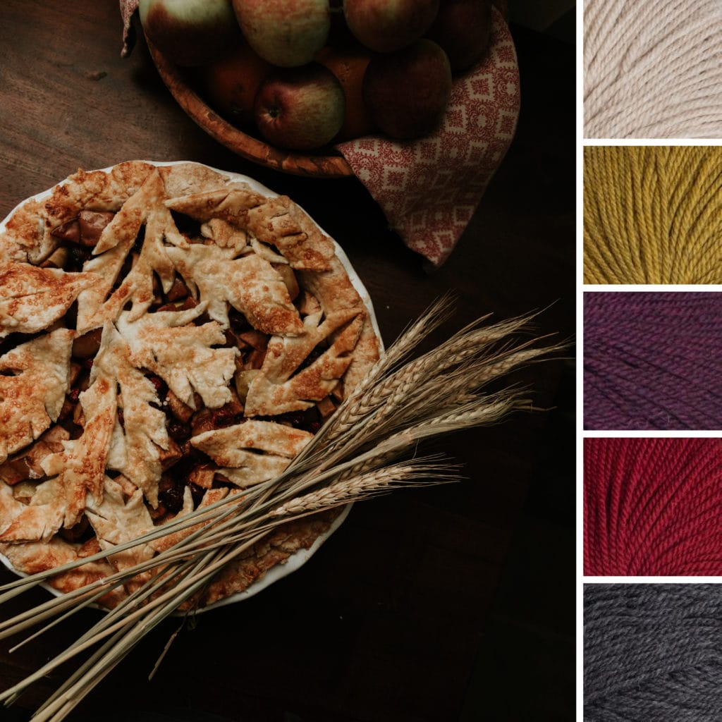 A top-down view of an autumn pie with a bunch of wheat. Yarn color palette is: oatmeal, yellow, black cherry, deep red, and charcoal gray.