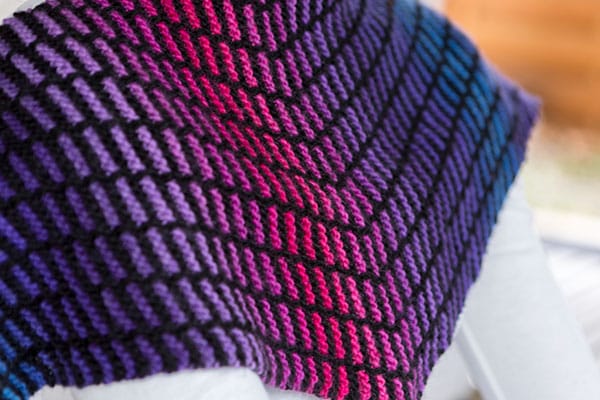 A closeup of a knitted shawl that features lines of gradient color in a field of black.