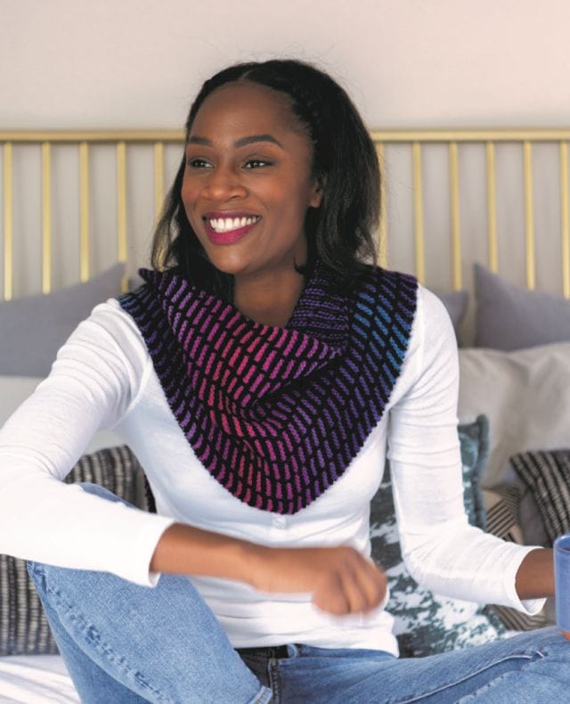 A model wears a knitted shawl around her neck that features lines of gradient color in a field of black.