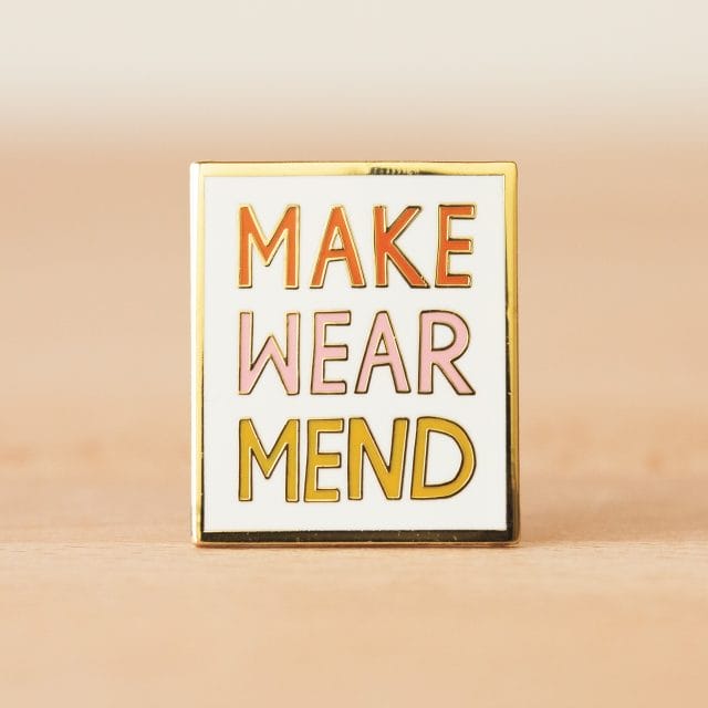An enamel pin that says "Make Wear Mend"