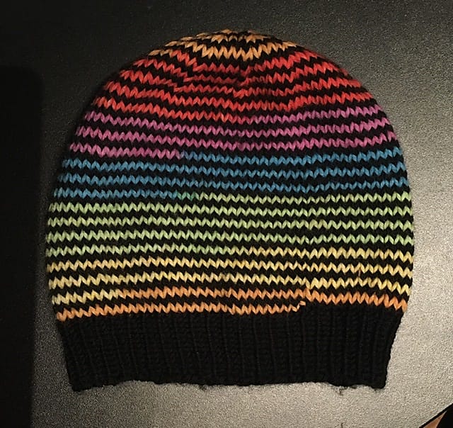 A black and rainbow striped knitted hat by Rachel Luxemburg.