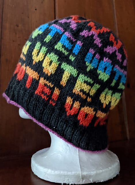 Ballot Box Beanie by Rachel Luxemburg. A black knitted hat that says "VOTE!" in rainbow repeat.