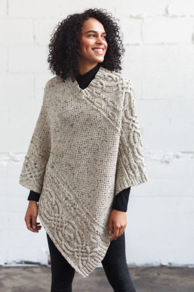 Big poncho modeled on woman, with cables along upper right side and lower left side, and textured fabric in the center