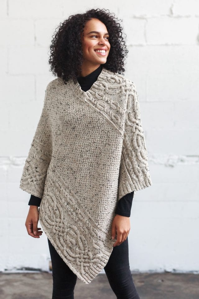 Big poncho modeled on woman, with cables along upper right side and lower left side, and textured fabric in the center