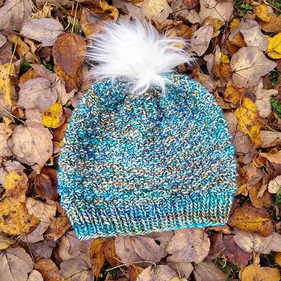 A multicolored blue knitted hat with a white fur pom-pom