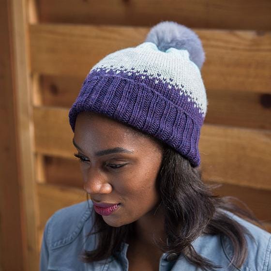 A purple knit cap that transitions to light blue, topped with a lavender fur pom-pom