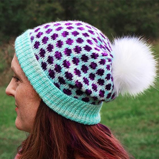 an aqua knitted hat with purple polka-dots and a white fur pom-pom