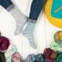 Top down view of hand-knit socks on a white sheet, surrounded by colorful yarns and sock knitting accessories.