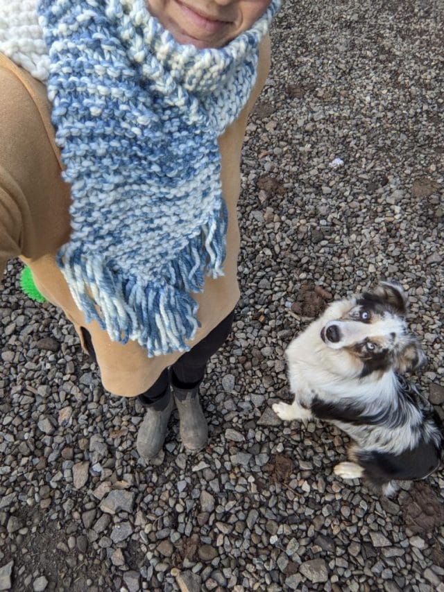 Hillary doing a selfie of an indigo dyed knitted scarf along with her dog who is looking at the camera